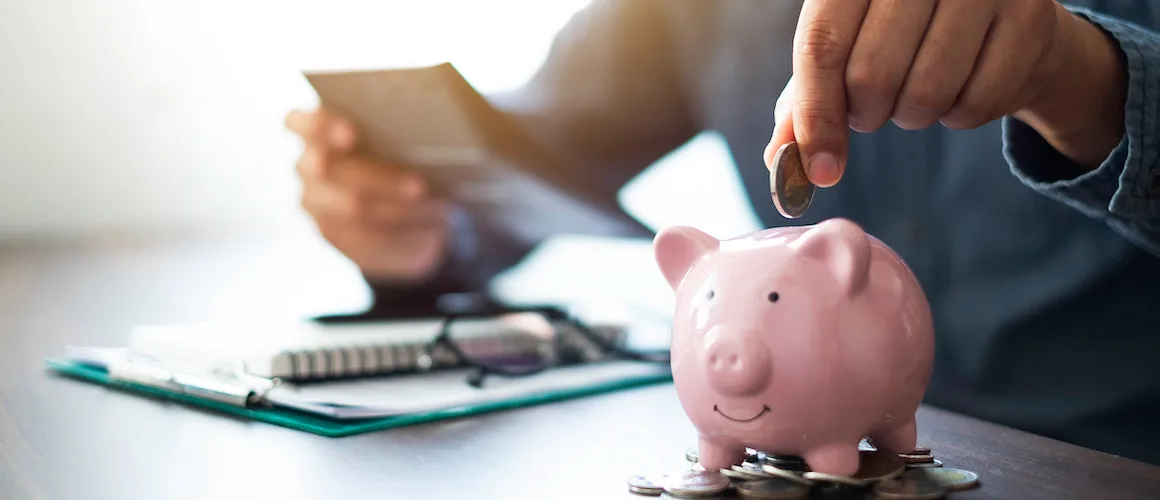 Close-up image of man hand putting coins in pink piggy bank for account save money.